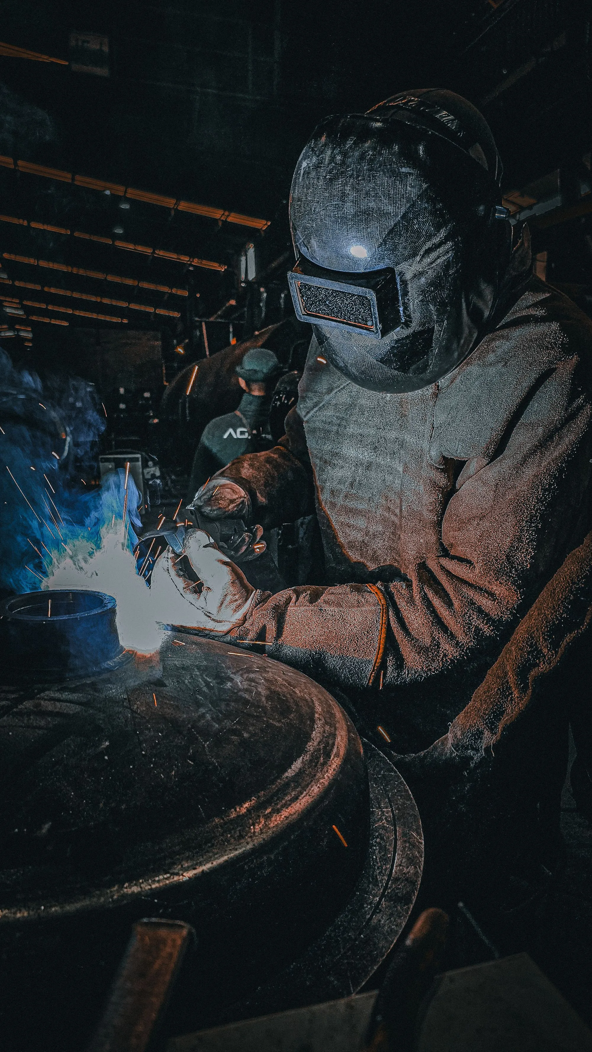 Welder wearing protective clothing and a welding helmet during metal fabrication